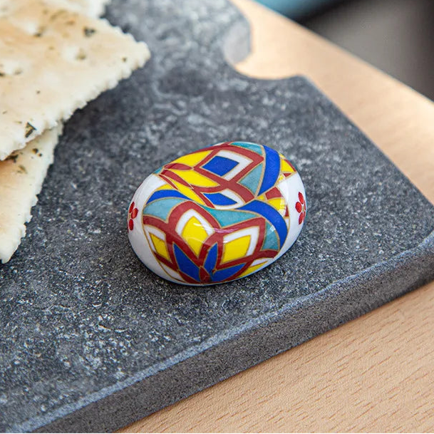 Colorful ceramic kawaii chopstick holder on a dark stone surface with crackers