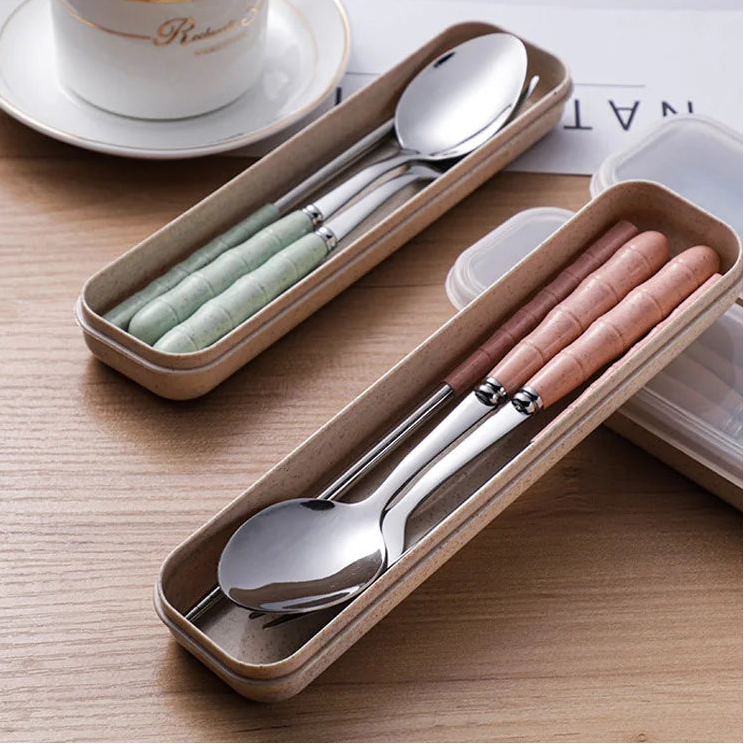 Set of silver kawaii utensils in a beige carrying case on a wooden surface with a cup of coffee in the background.
