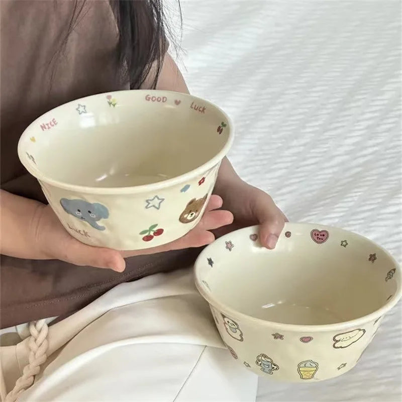 Two ceramic kawaii ramen bowls with cartoon designs held by a person on a white background