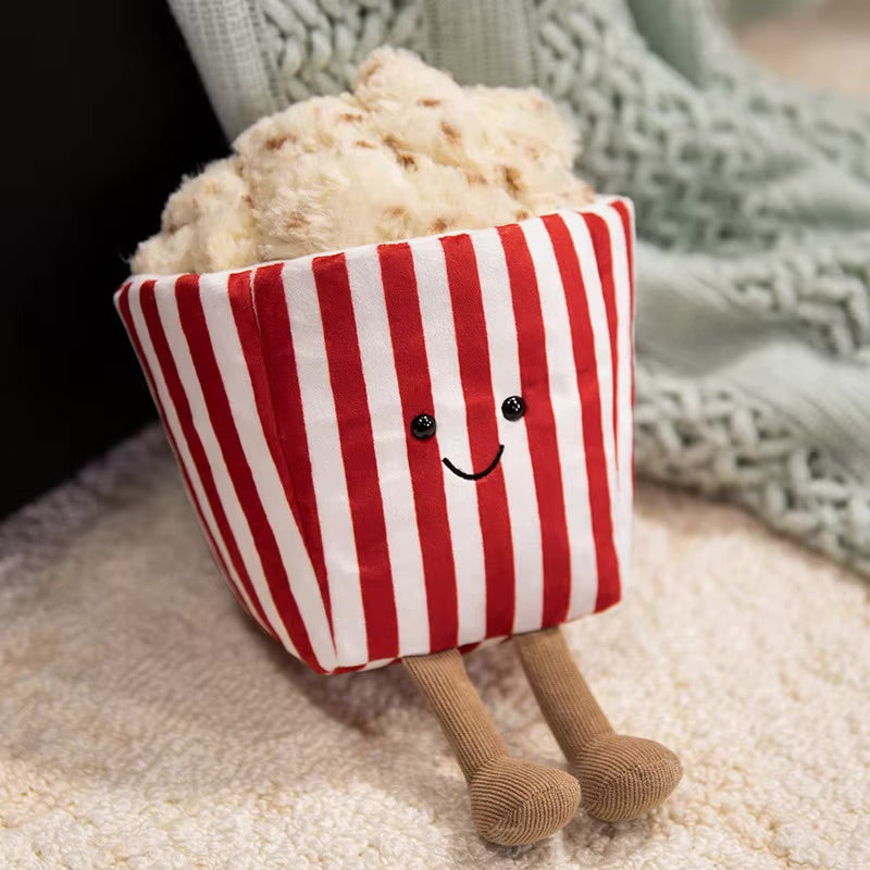 Kawaii plush toy resembling a popcorn bucket with legs and a smiling face on a blanket.