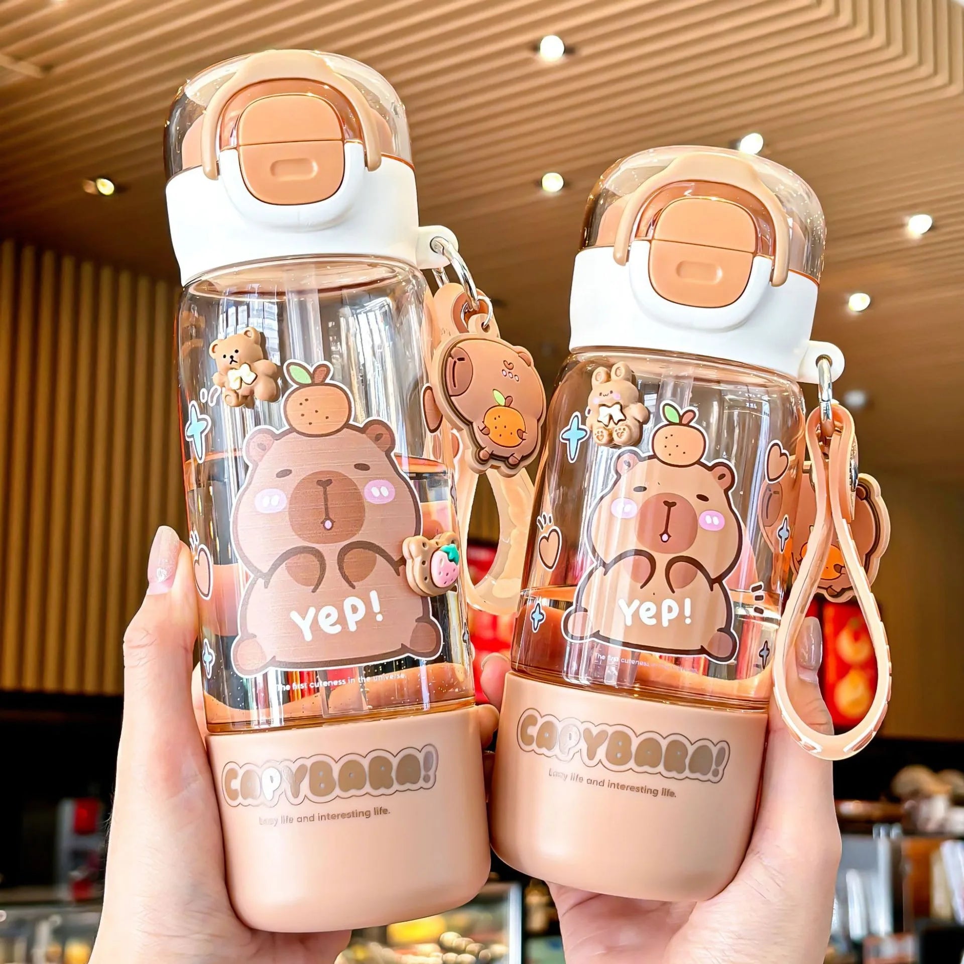 Two bear-themed kawaii water bottles held by a person in an indoor setting.