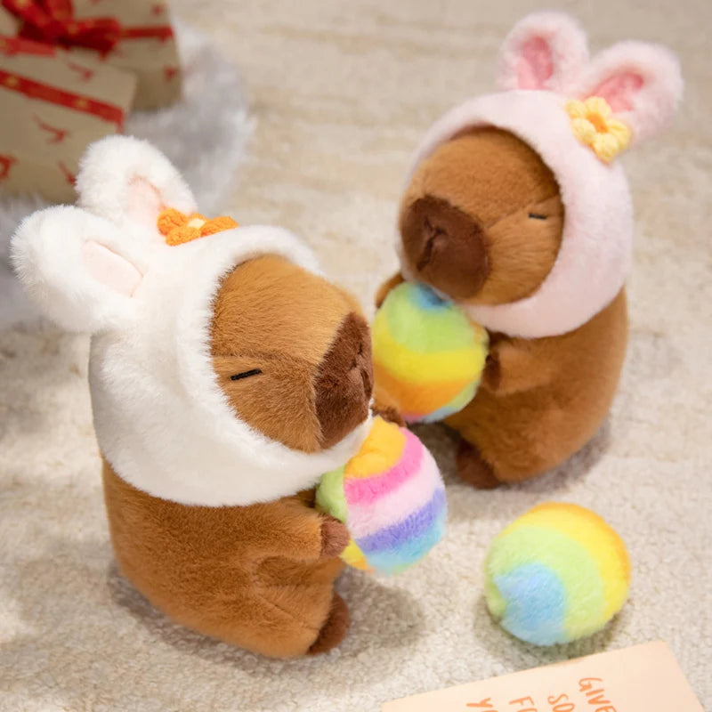 Two brown kawaii plush toys with white hats holding rainbow-colored balls on a beige surface.