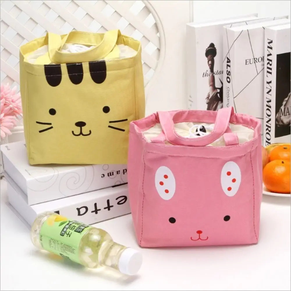 Two cartoon-themed kawaii lunch bags, one yellow and one pink, on a surface with books and a bottle.