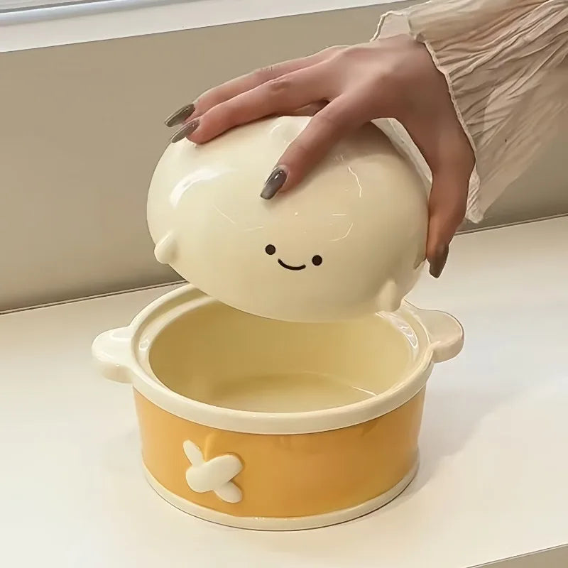 Hand holding a cute, cartoonish ceramic kawaii ramen bowl with a smiling face on a white surface.