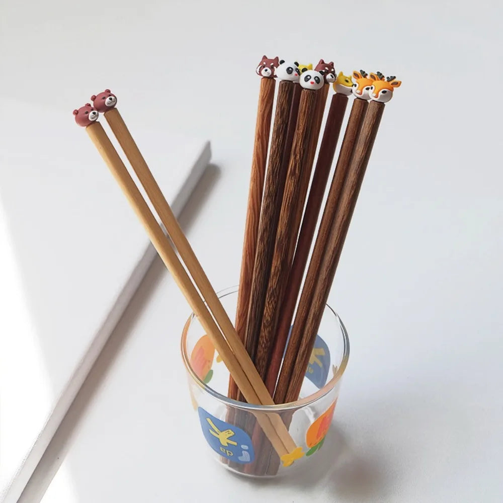 Set of wooden kawaii chopsticks with animal-shaped tips in a glass holder on a white background