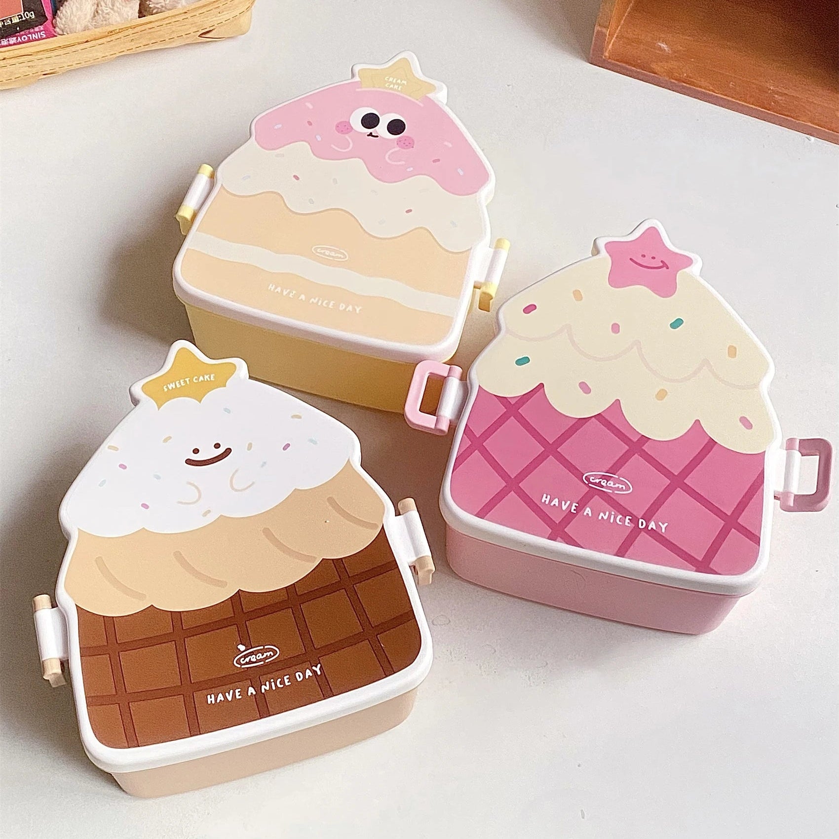 Three ice cream-themed kawaii bento boxes on a light surface with a wooden shelf in the background.