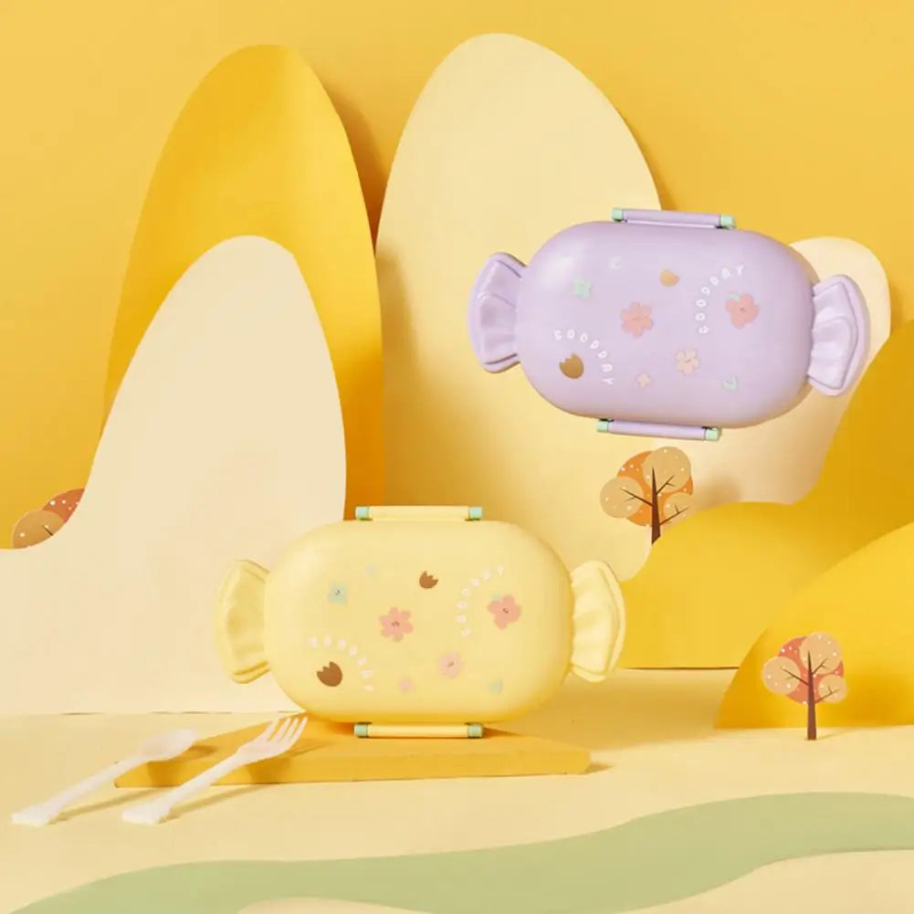 Two cartoon-style kawaii lunch boxes on a yellow landscape with trees and grass.