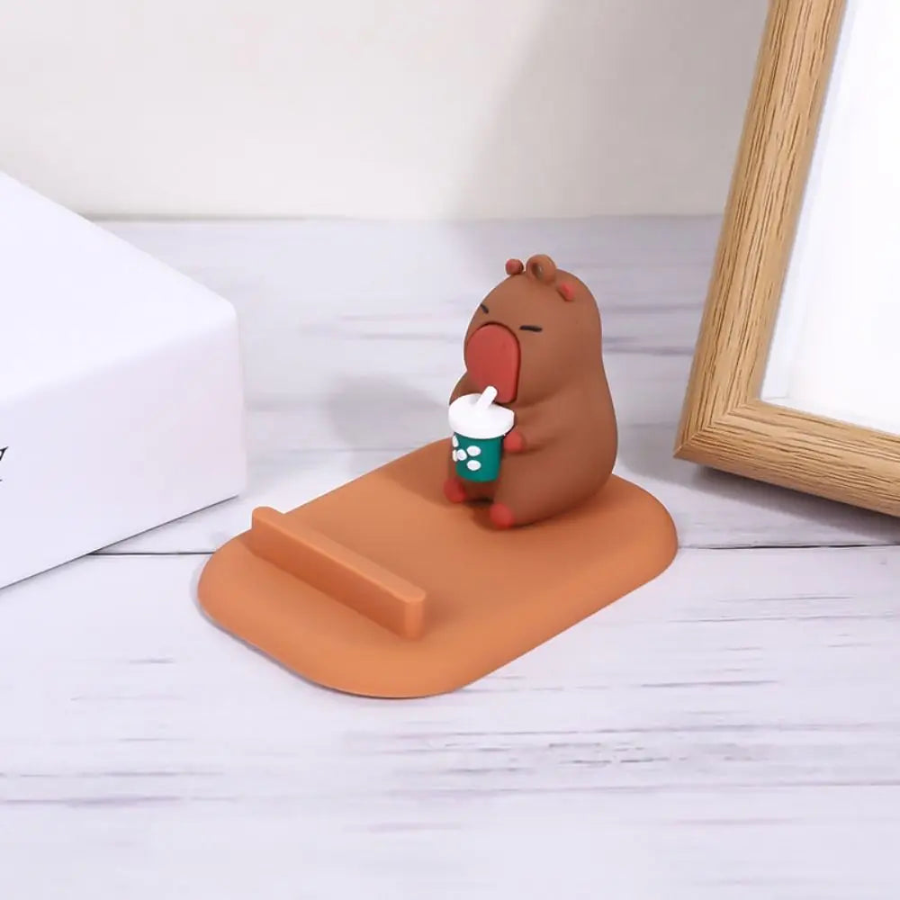 Brown kawaii capybara phone holder with a white shirt on an orange stand against a light background