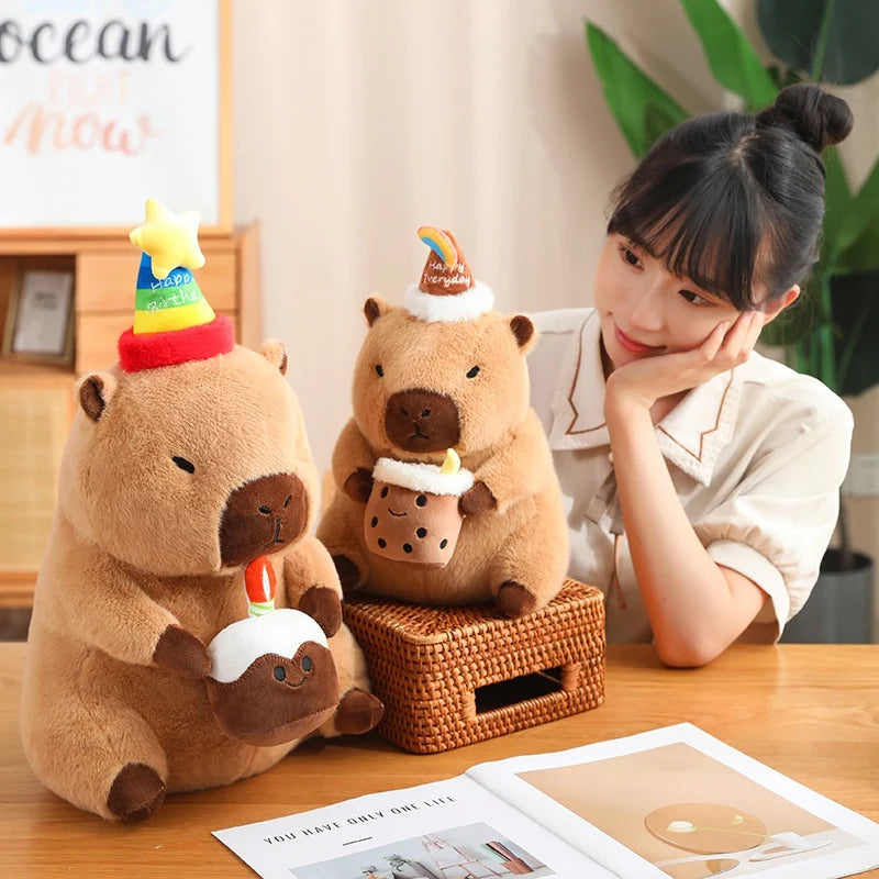 Two capybara plush toys with birthday hats on a table next to a person.
