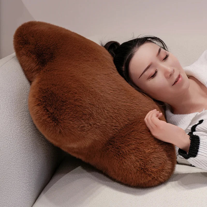 A woman rests her head on a large, plush, brown faux-fur shaped pillow on a light gray sofa.