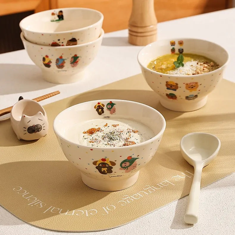 Ceramic kawaii ramen bowls with cartoon designs on a table with a placemat and spoon.
