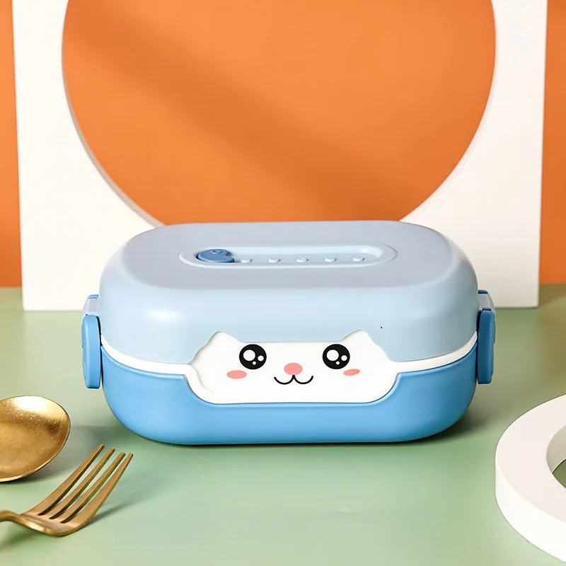 Blue kawaii lunch box with a cute face design on a green surface with a gold fork and white plate.