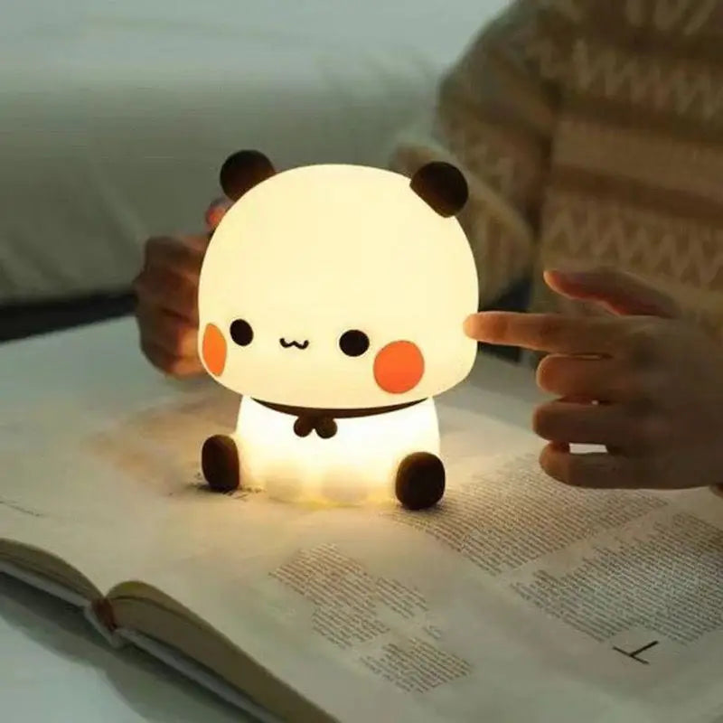 Cute panda-shaped kawaii night light on an open book with a person's hand pointing at it.
