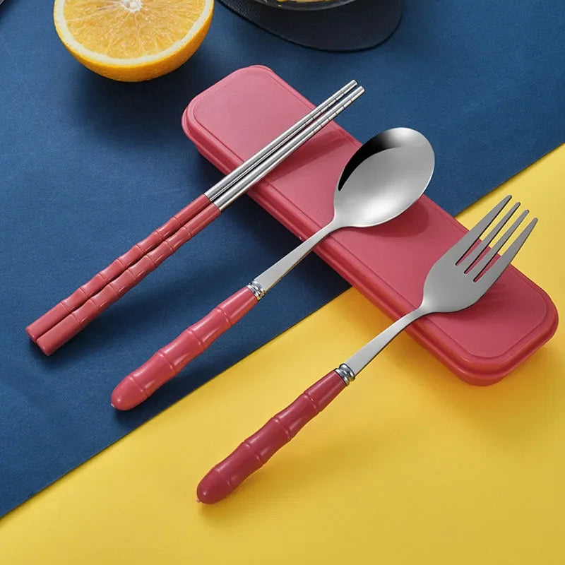 Stainless steel kawaii utensils set with red handles on a blue and yellow background, featuring a half lemon and a bowl of fruit.