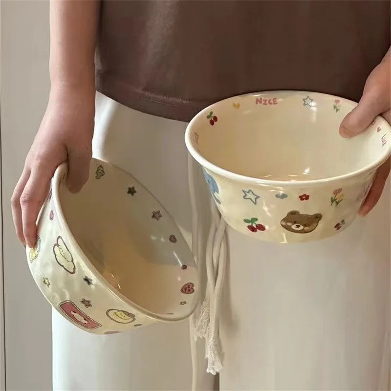 Two ceramic kawaii ramen bowls with cartoon designs held by a person against a neutral background