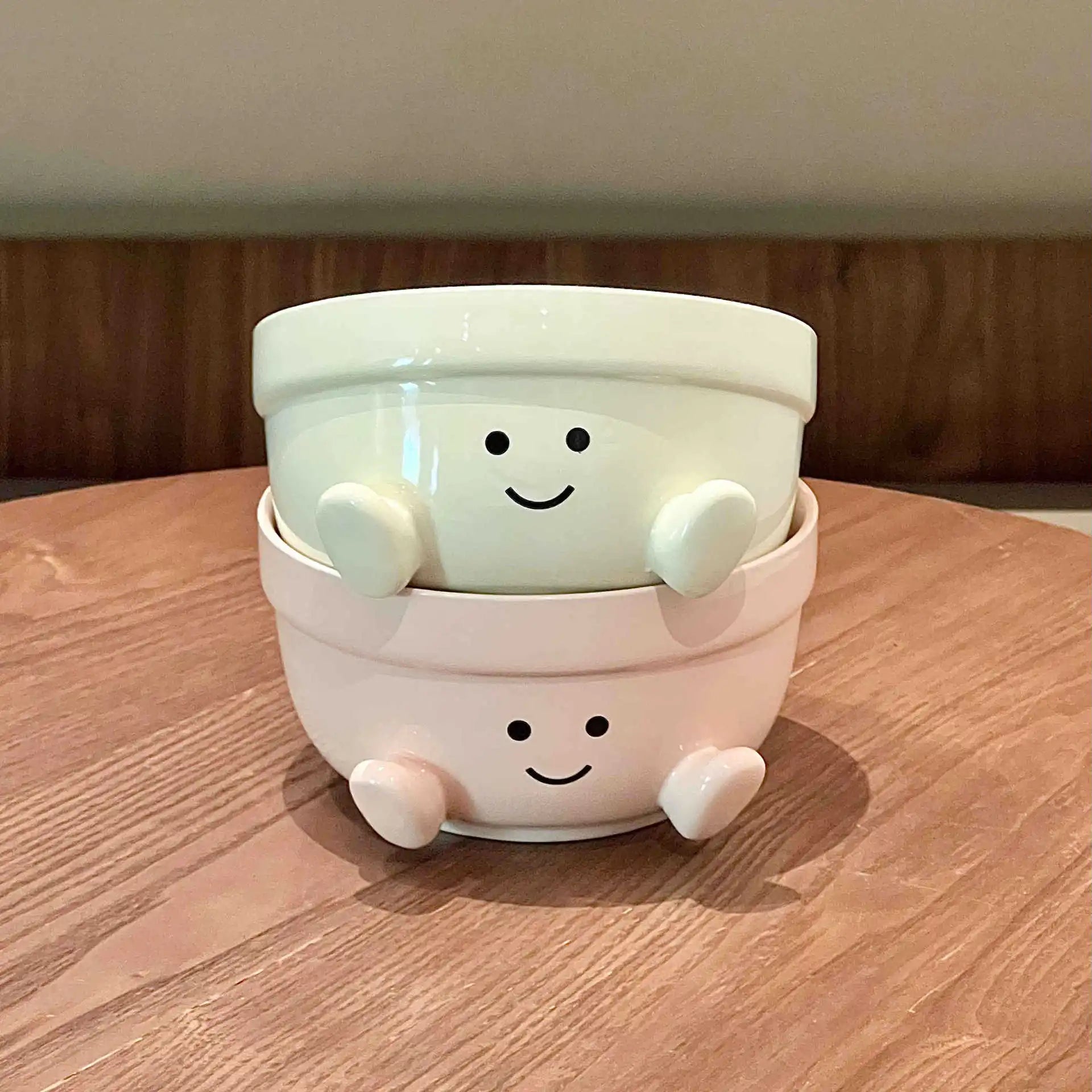 Two white ceramic kawaii bowls with smiley face design stacked on a wooden surface.