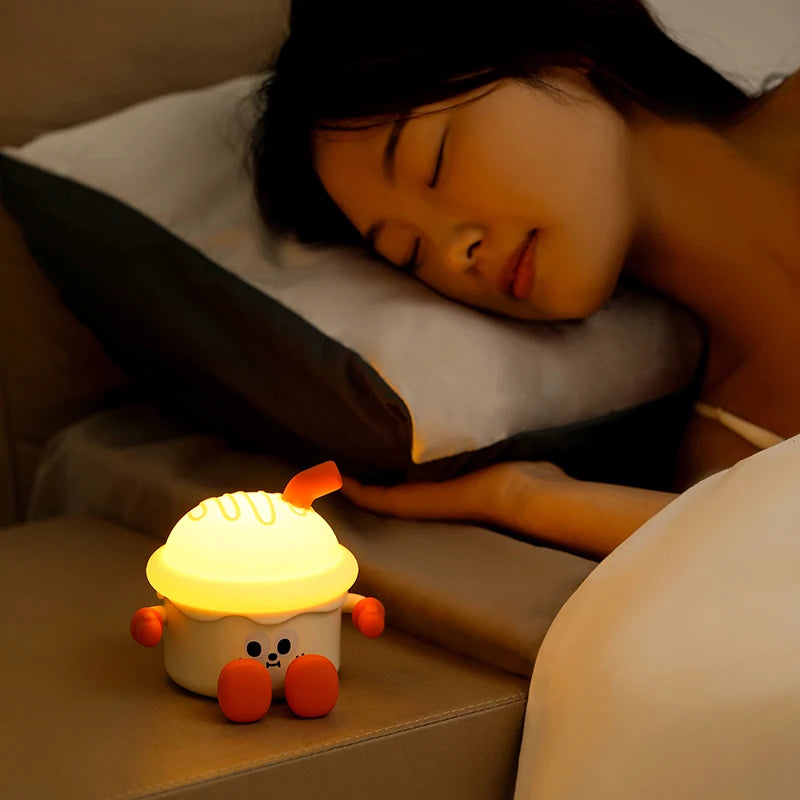 Person lying down with a glowing plush kawaii night light on a surface.