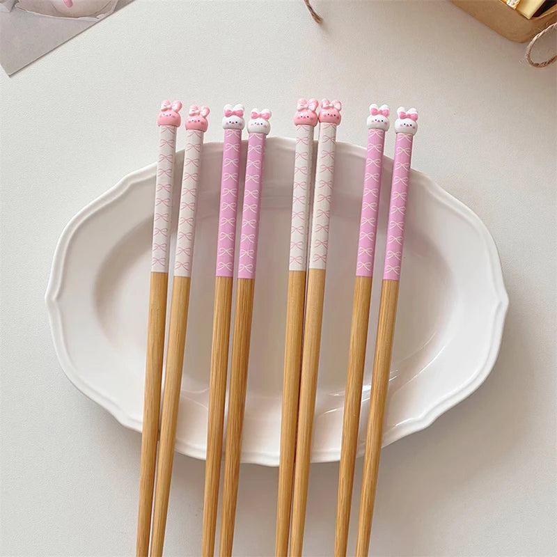 Set of five pink and gold kawaii chopsticks with decorative ends on a white plate.