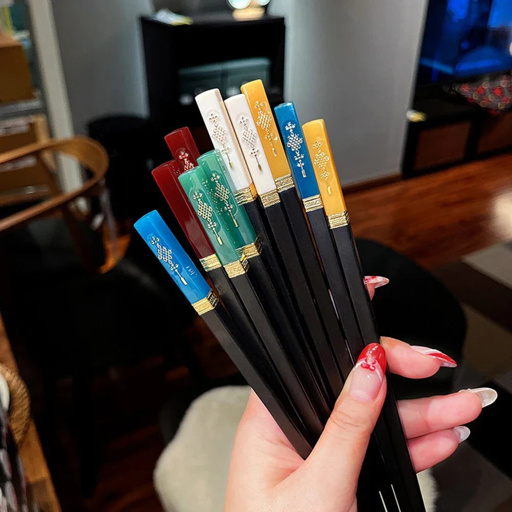 Set of black kawaii chopsticks with colorful handles held by a hand in a casual indoor setting.