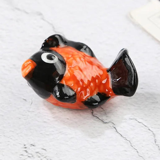 Small black and orange fish-shaped kawaii chopstick holders on a light gray surface with text overlay.