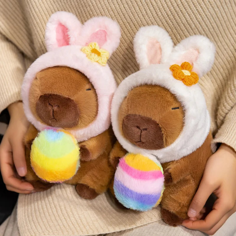Two kawaii plush toys resembling bunnies with colorful eggs held by a person wearing a beige sweater.