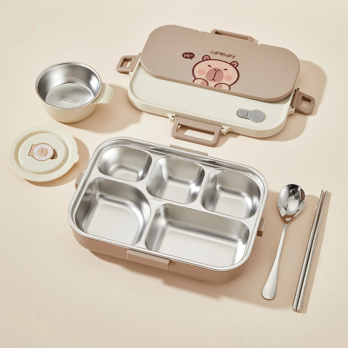 Kawaii-style lunch box set with compartments, bowl, spoon, and chopsticks on a beige background