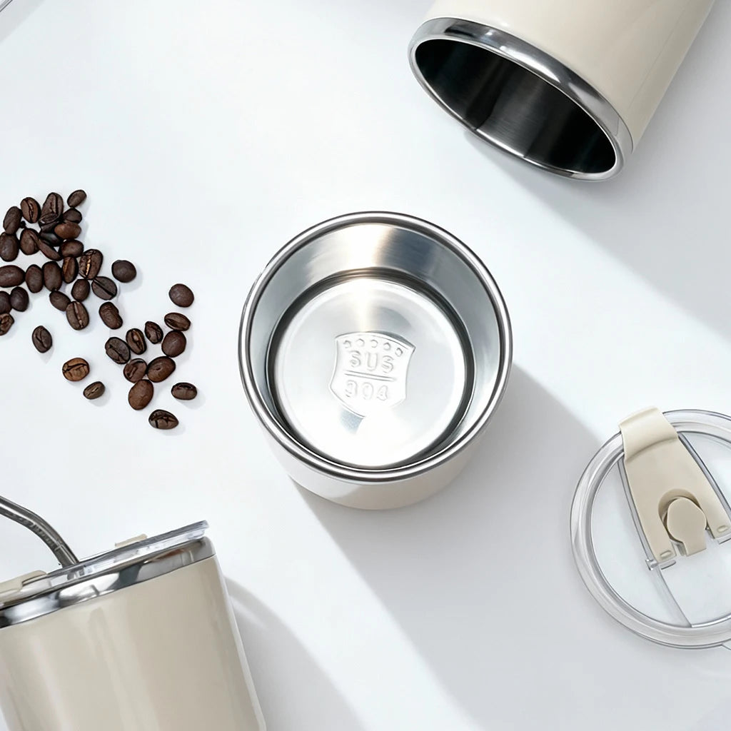 Stainless steel kawaii tumbler with beige lid on a white surface with coffee beans.