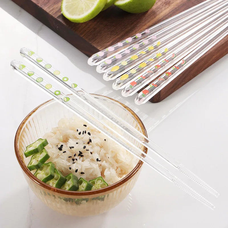 Clear kawaii chopsticks with colorful dots on a white surface next to a bowl of rice and vegetables.