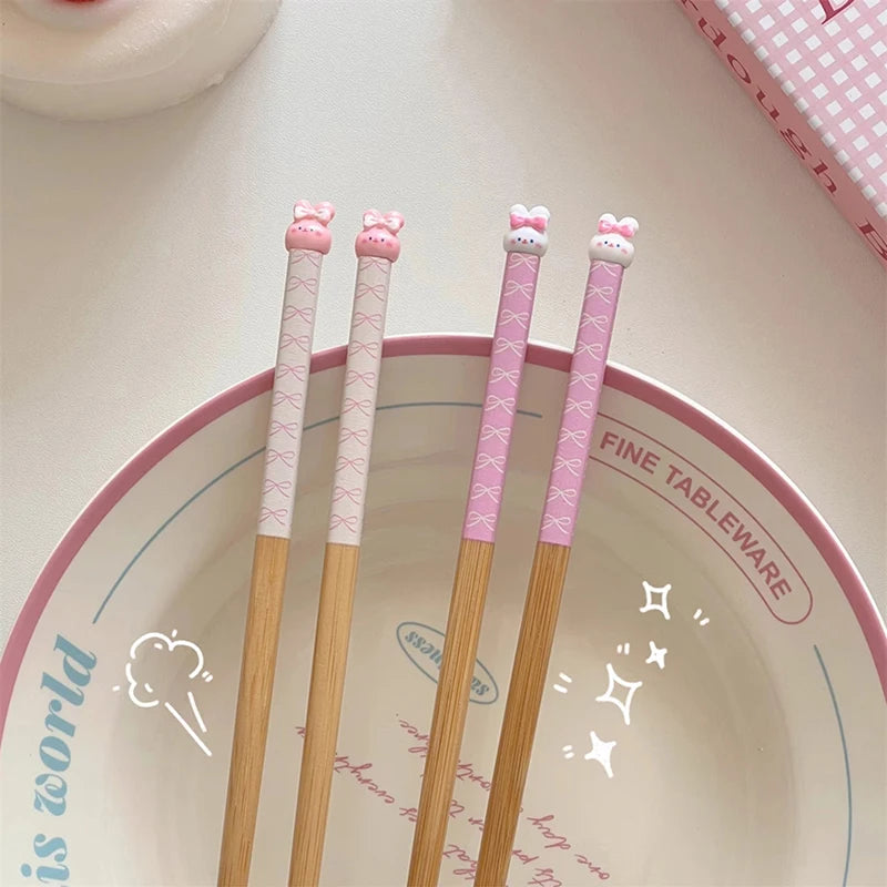 Set of wooden kawaii chopsticks with pink handles featuring cat designs on a ceramic plate.