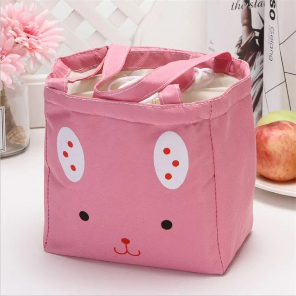 Pink kawaii bag with a cartoon face design on a white surface with flowers and an apple in the background.