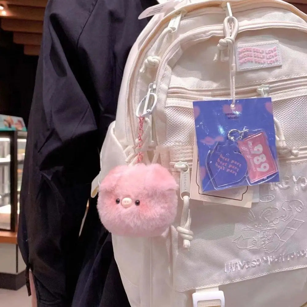 Pink fluffy kawaii keychain attached to a backpack with a visible brand tag.