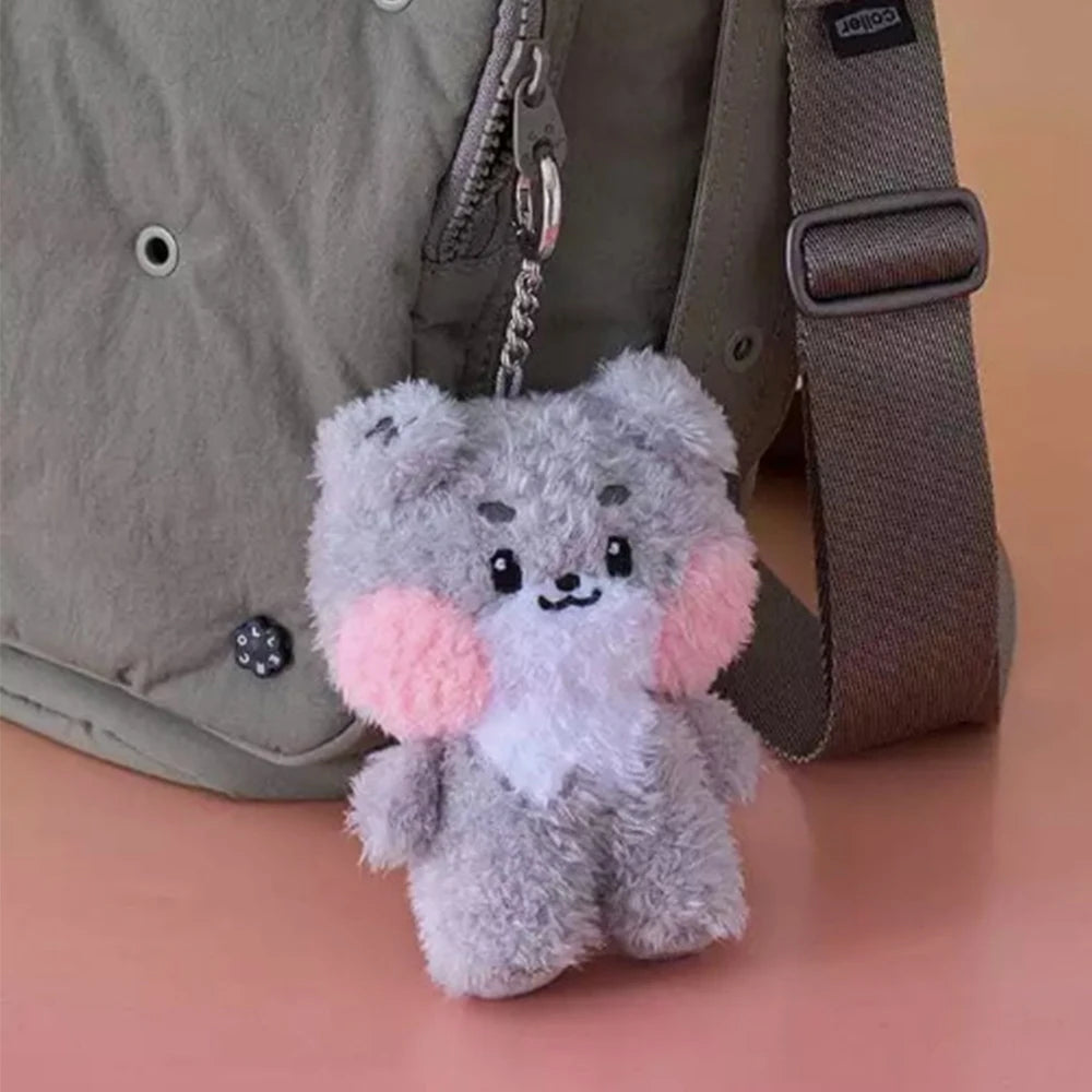 Gray kawaii plush keychain with pink accents attached to a green bag.