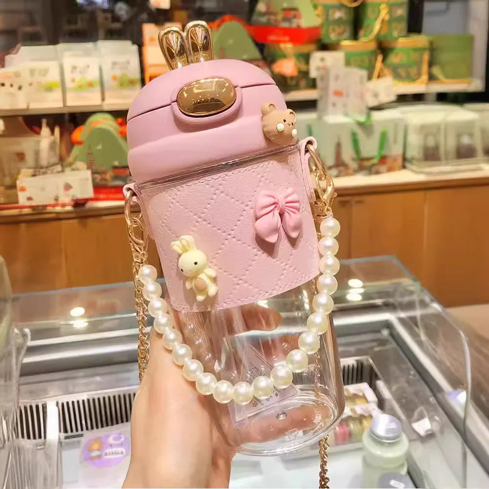 Pink kawaii water bottle with decorative elements held in a hand, blurred store interior in the background