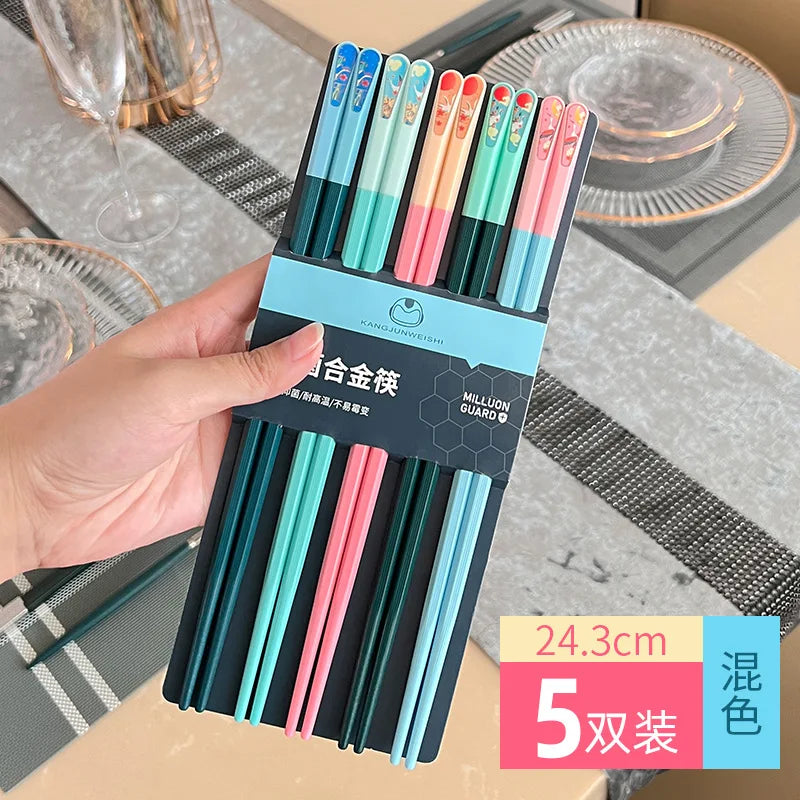 Set of colorful kawaii chopsticks in packaging held by a hand with a table setting in the background.