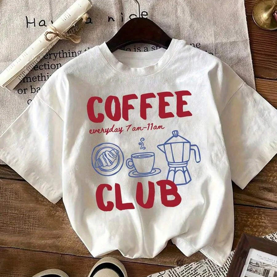 White t-shirt with 'Coffee Club' text and kawaii graphics on a wooden surface.