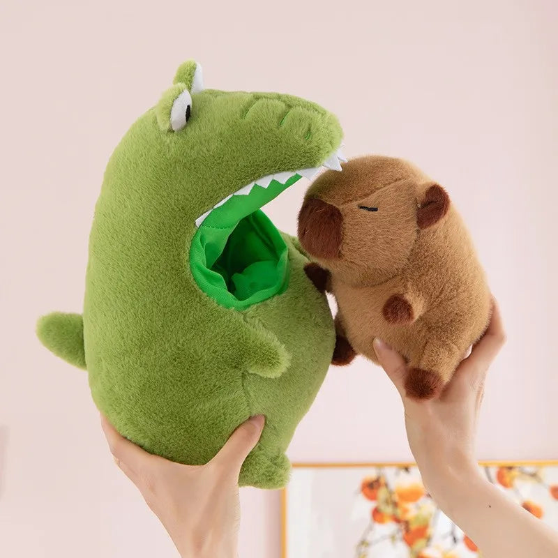 Green kawaii plush toy with a mouth opening, holding a small brown plush animal against a light pink background.