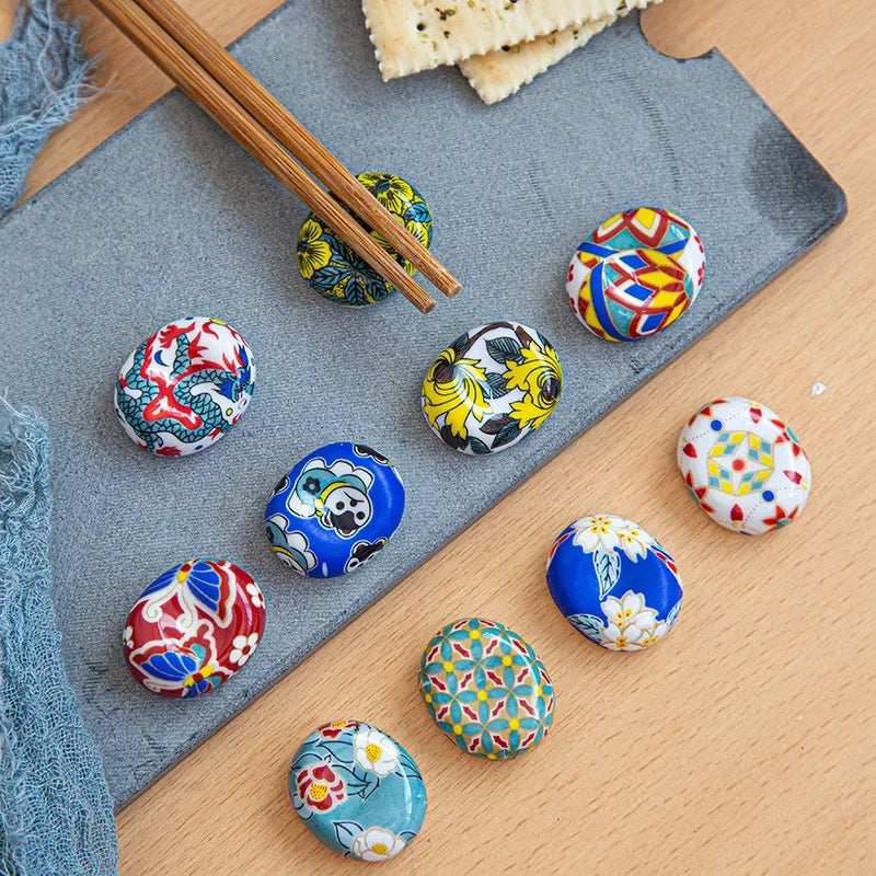 Colorful ceramic kawaii chopstick holders on a wooden surface with a gray mat and chopsticks.
