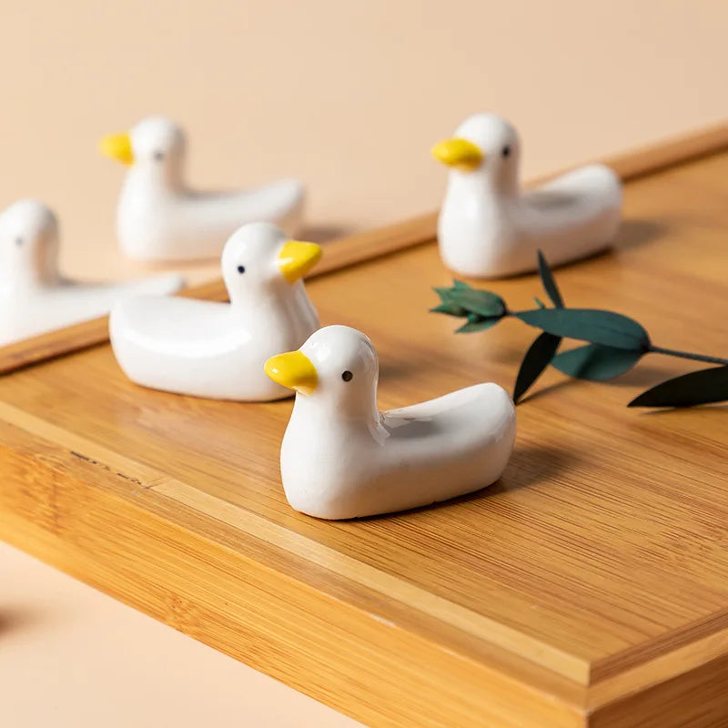 White ceramic duck kawaii chopstick holders with yellow beaks on a wooden surface.