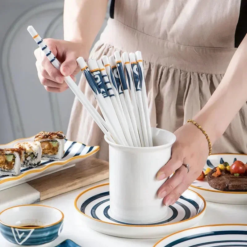 Person holding a set of kawaii chopsticks over a white container with more chopsticks, surrounded by food on a table.