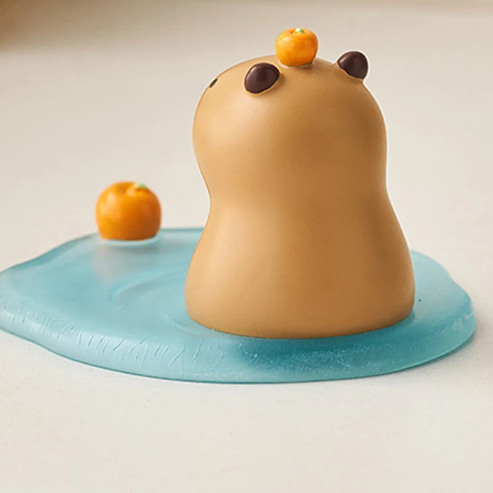 Kawaii phone holder of a capybara with orange eyes and ears on a blue platform with oranges around, on a light beige background