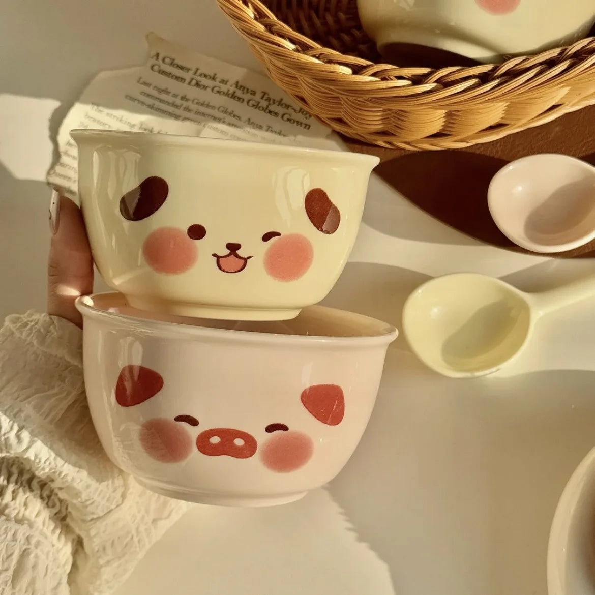 Two small ceramic kawaii ramen bowls with cartoon face designs held by a hand on a light surface.