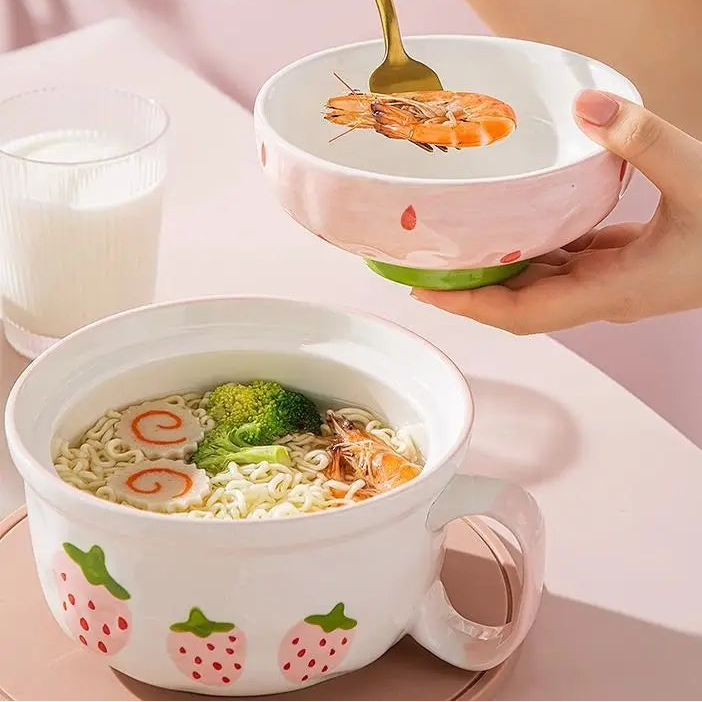 Two kawaii bowls with a lid, one being held with a spoon, on a pink background.