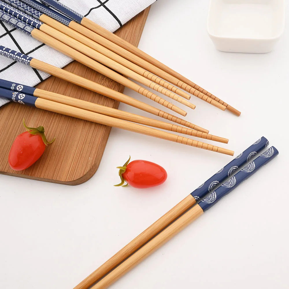 Set of wooden kawaii chopsticks with decorative blue handles on a white surface with tomatoes and a cutting board.