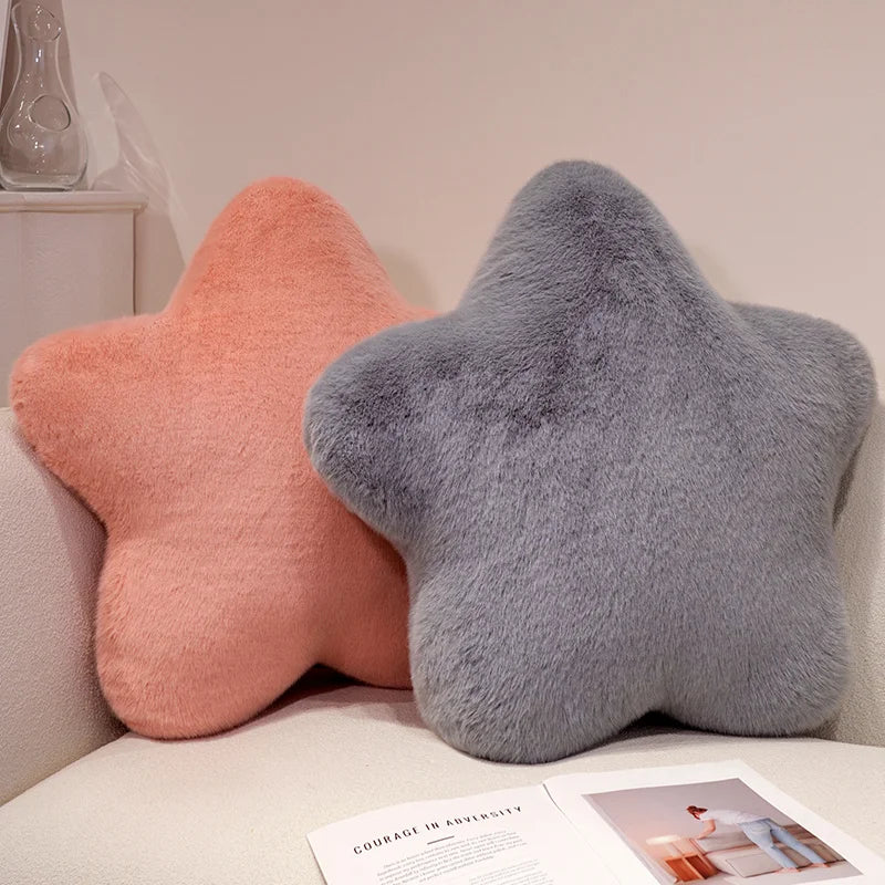 Two star-shaped cushions, one pink and one gray, on a couch with a magazine underneath.