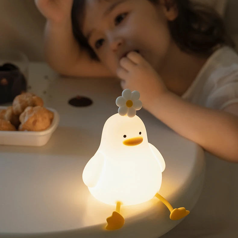 Child playing with a glowing duck-shaped kawaii night light on a surface.