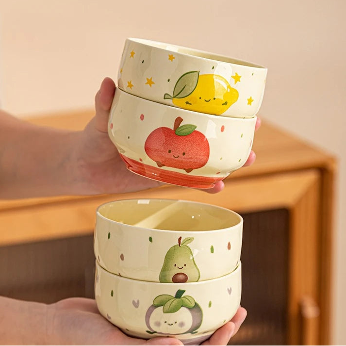 Stackable ceramic kawaii bowls with fruit designs held by a person.