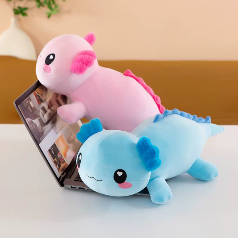 Two plush axolotl toys, one light pink and one light blue, styled on top of a laptop on a white table against a warm beige background.