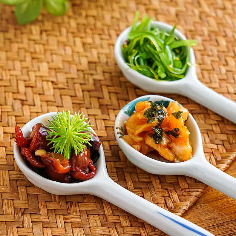 Three white ceramic kawaii spoons filled with various foods on a woven mat