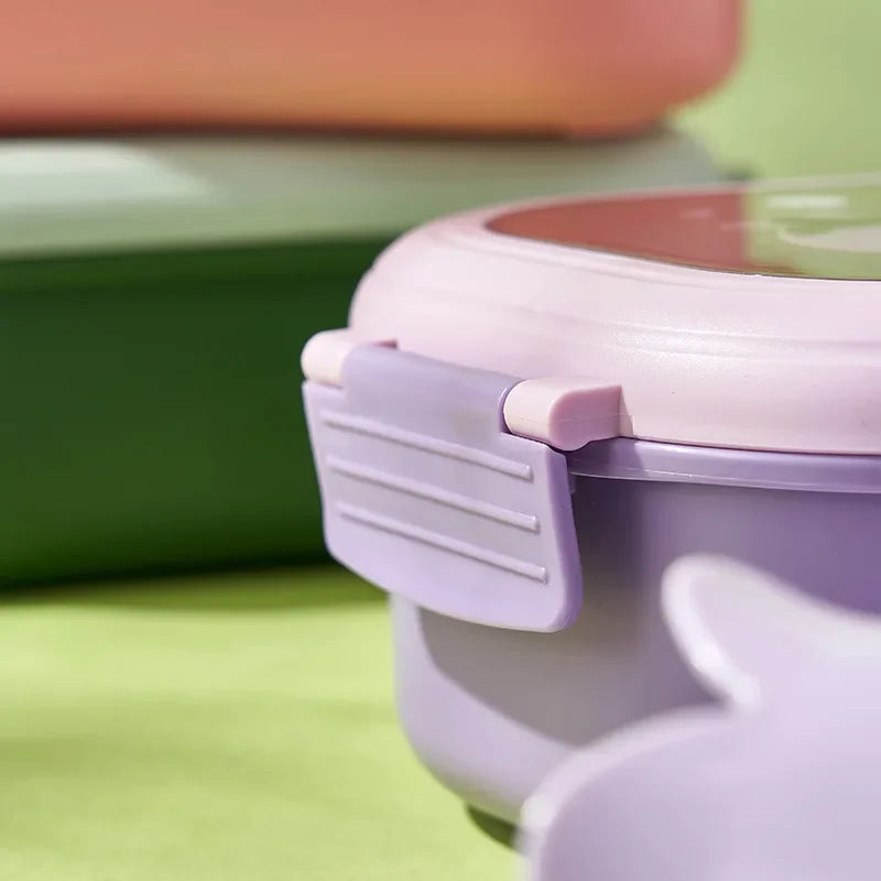 Close-up of a purple kawaii lunch box with a pink lid on a green surface