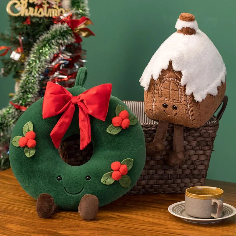 Decorative wreath and gingerbread house kawaii plush toys on a table with a Christmas tree in the background.
